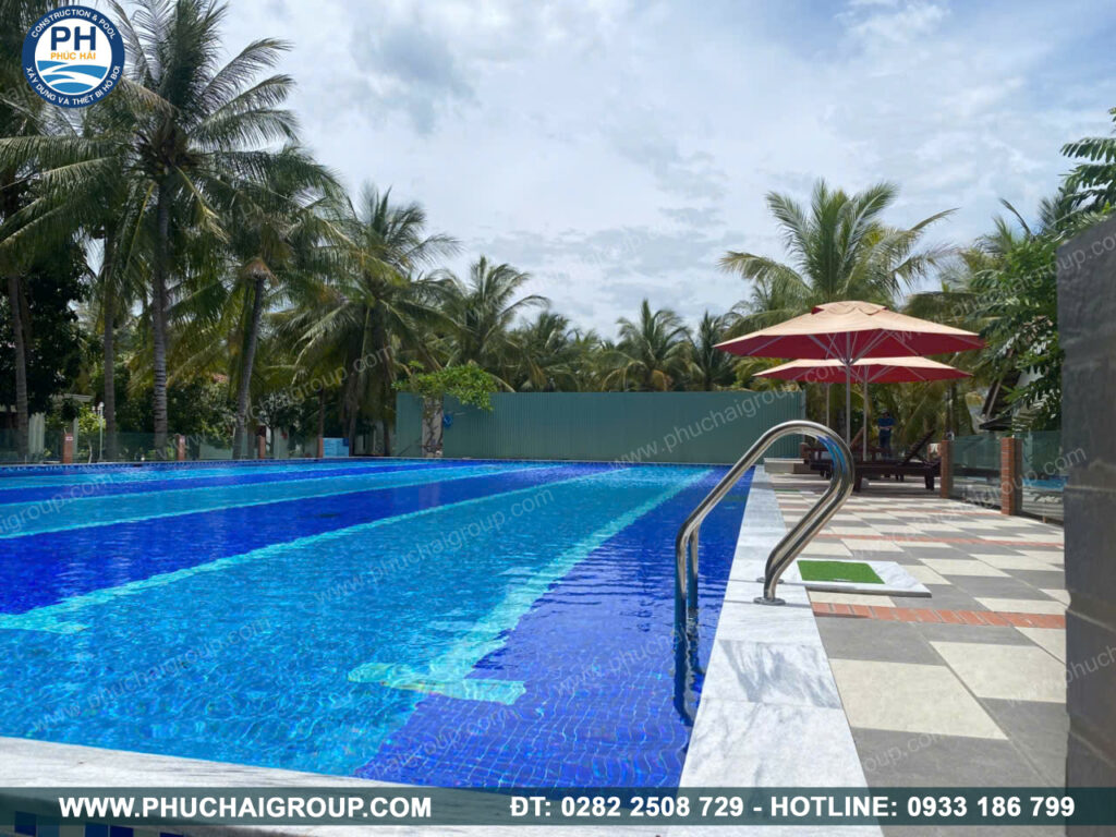 Không gian hồ bơi resort ngoài trời đạt chuẩn an toàn, trang bị lối đi chống trượt và ô che nắng tiện nghi